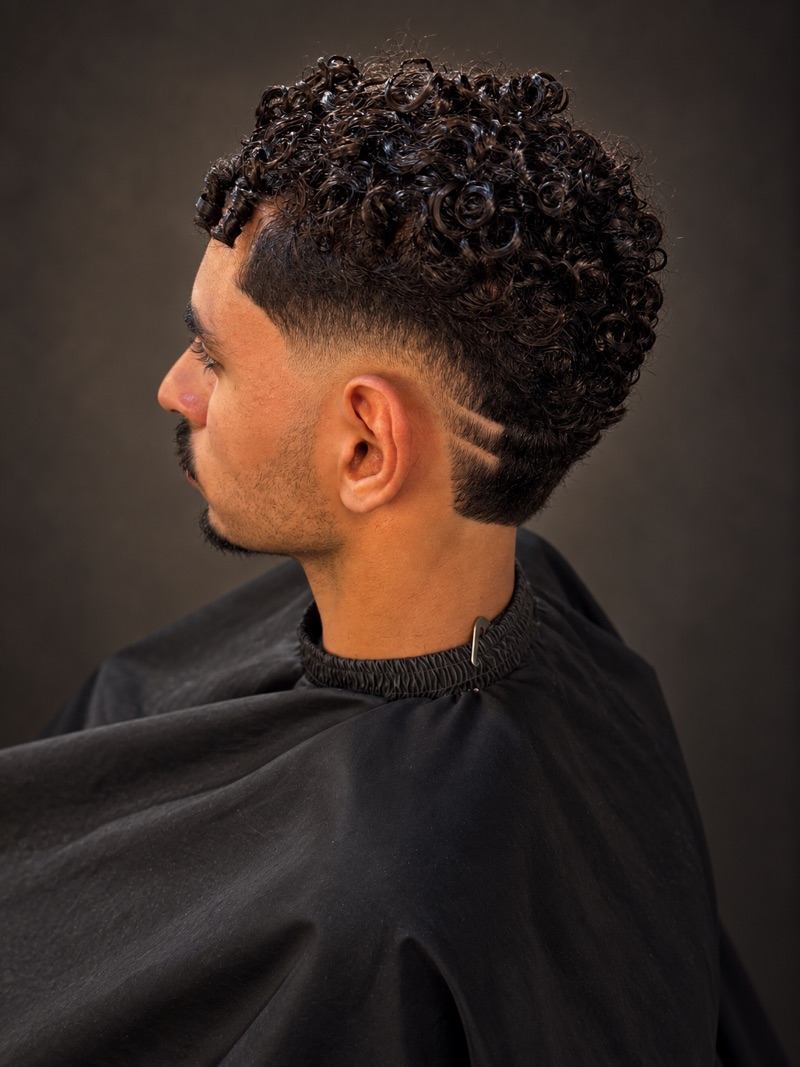 Cabello rizado con fade y líneas de diseño a navaja, vista de perfil